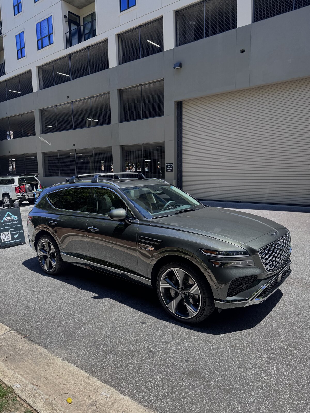 Detailed dark green Genesis GV80 SUV beside the Apex Mobile Detailing sign